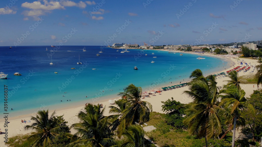 Obraz premium Aerial of the beautiful beach in Barbados. A view over palm trees on a beach, blue water and boats 