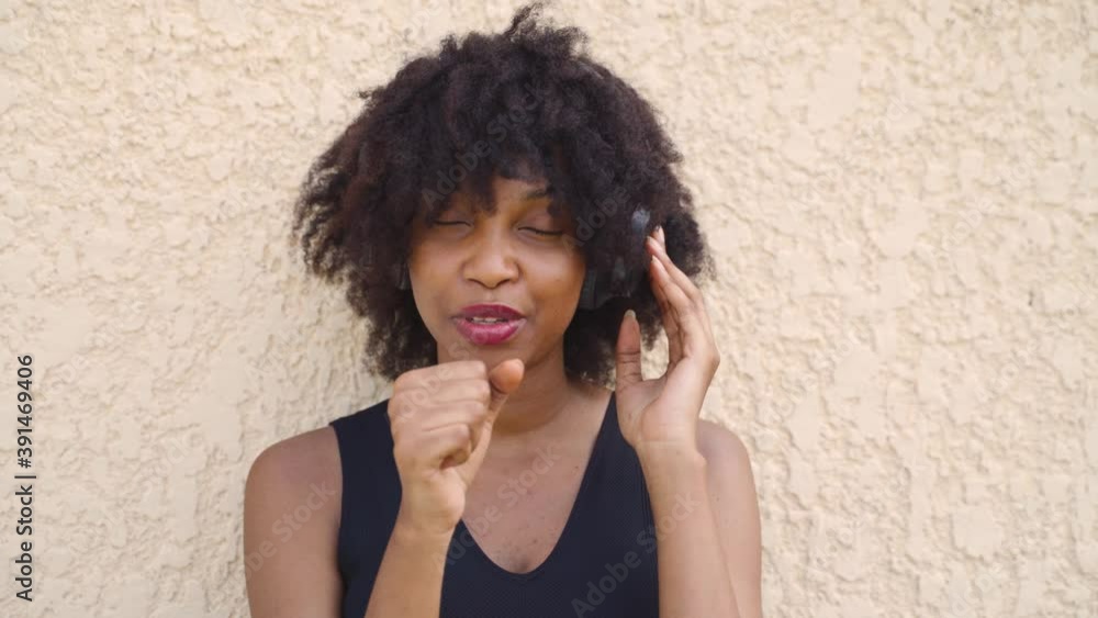 Young African American woman in afro hairstyle singing with headphones on the street. Female black singer listening to sound of music with happiness. - 4K Real Time Footage Young African American woman in afro hairstyle singing with headphones on the street. Female black singer listening to sound of music with happiness. - 4K Real Time Footage