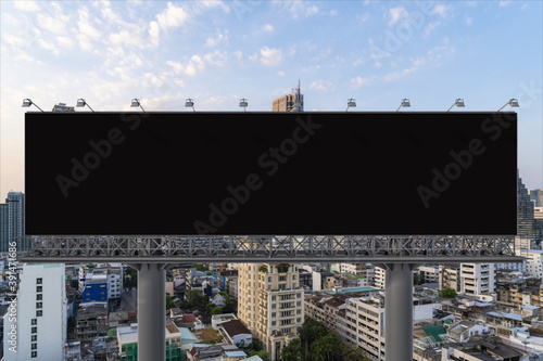 Blank black road billboard with Bangkok cityscape background at sunset. Street advertising poster, mock up, 3D rendering. Front view. The concept of marketing communication to promote or sell idea.