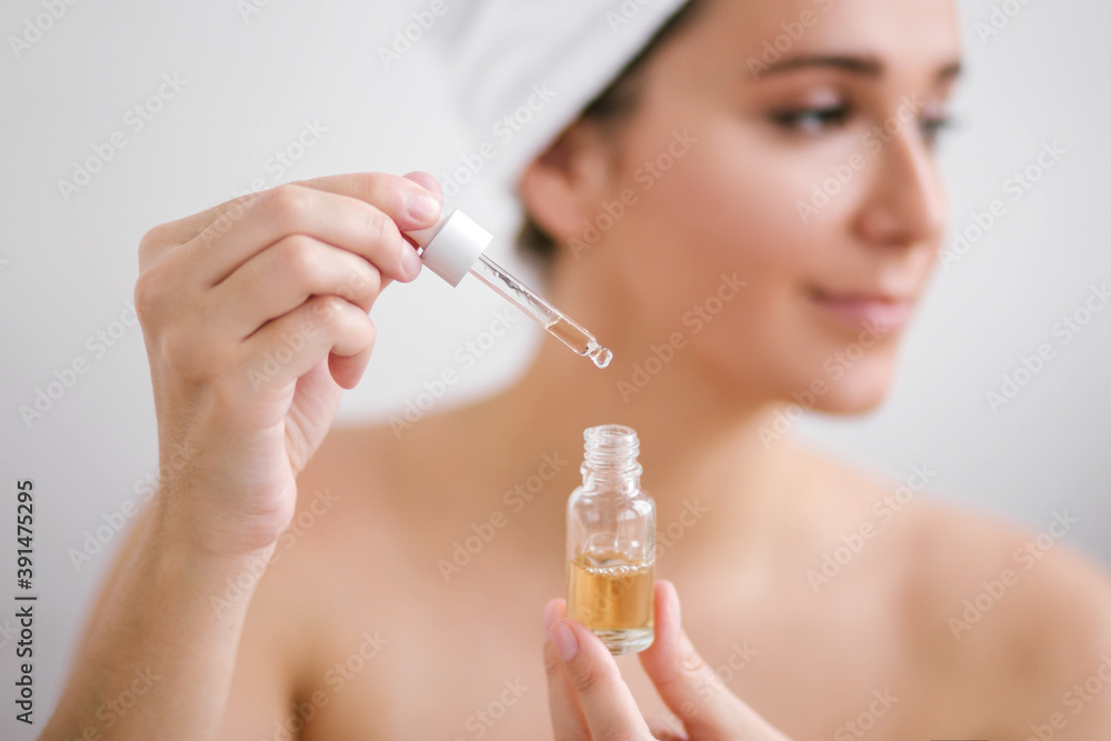 Portrait of beautiful young woman with towel on head holding face oil. Portrait of beautiful young woman with towel on head holding face oil.