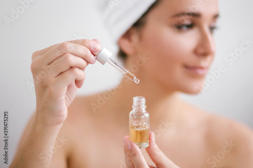 Portrait of beautiful young woman with towel on head holding face oil.