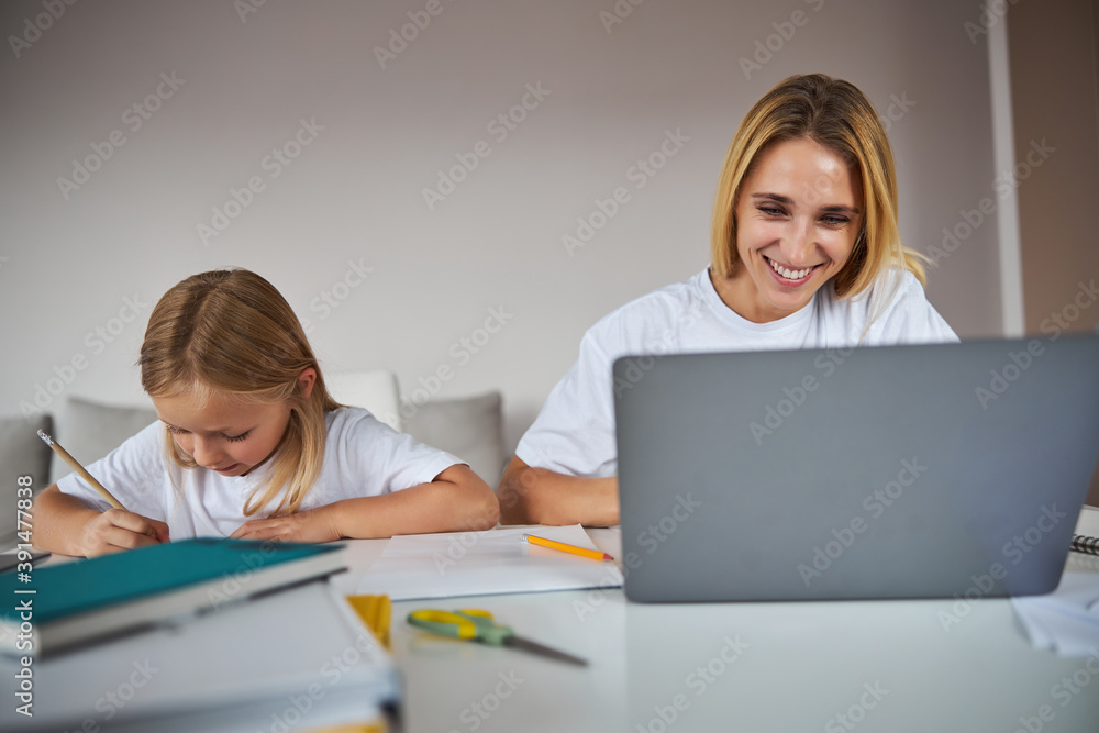 Business woman doing work tasks on a laptop while little girl sitting near her at the book Business woman doing work tasks on a laptop while little girl sitting near her at the book