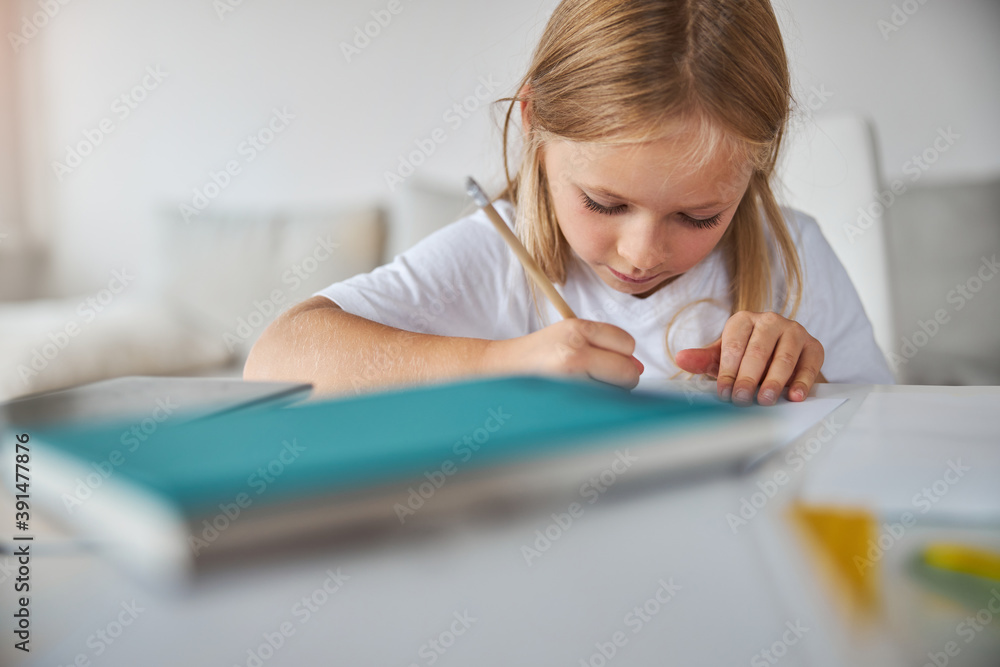 Thoughtful small miss writing letter at the table in room inside Thoughtful small miss writing letter at the table in room inside