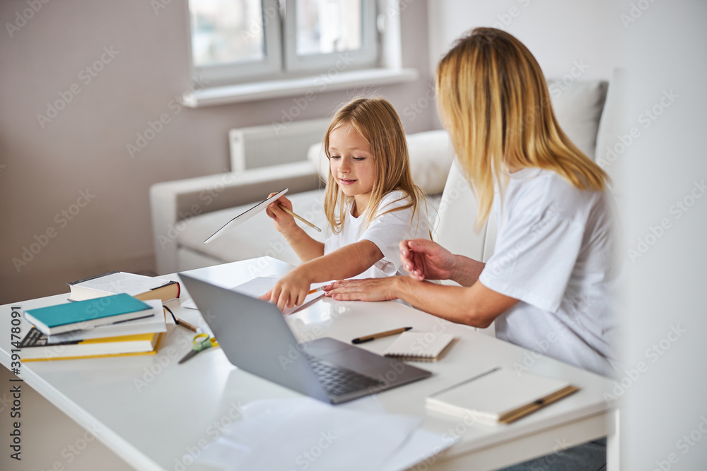 Image of workflow attractive charming female and small miss at the white table in room inside Image of workflow attractive charming female and small miss at the white table in room inside