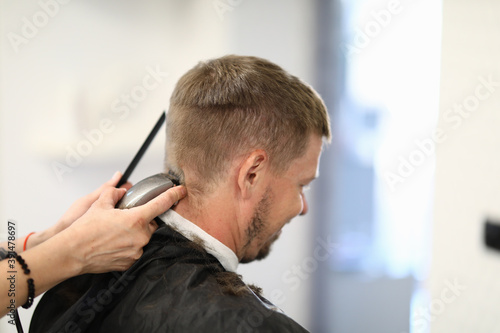 Man sits with his back master hairdresser cuts his hair with machine. Services and maintenance in beauty salons concept