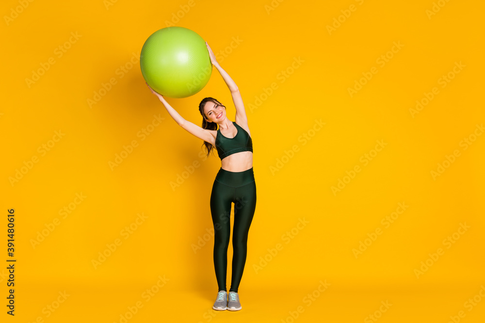 Full length body size view of nice cheery girl holding in hands fitball doing side incline isolated over bright yellow color background Full length body size view of nice cheery girl holding in hands fitball doing side incline isolated over bright yellow color background