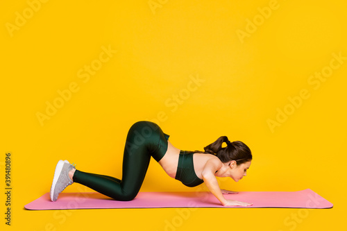 Profile side full body view of attractive thin slender bendy slim girl doing mat work out isolated on bright yellow color background