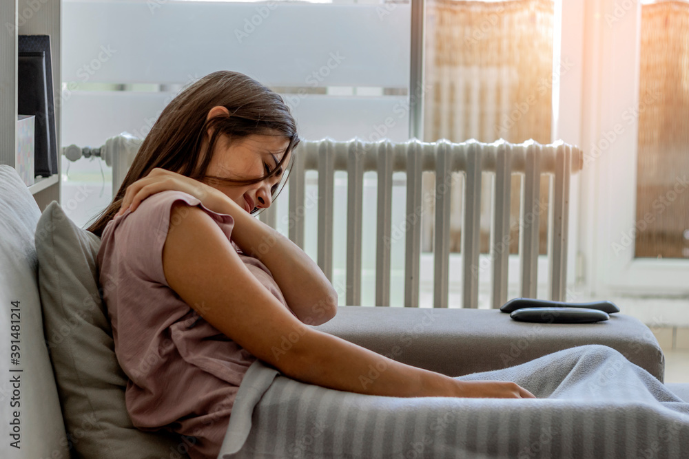 Portrait of a pretty young woman suffering from neck pain at home in the living room.Unhappy girl suffering from neck pain at home.Shot of an attractive young woman experiencing neck and shoulder pain Portrait of a pretty young woman suffering from neck pain at home in the living room.Unhappy girl suffering from neck pain at home.Shot of an attractive young woman experiencing neck and shoulder pain