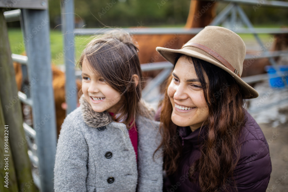 Fototapeta premium Smiling mother and daughter looking at the distance with alpacas behind them