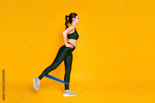 Profile photo of sporty lady gym training stretch rubber stripe legs wear sports suit isolated yellow color background