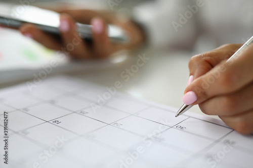 Woman's hand holds pen and marks calendar. Business calendar and task scheduling concept