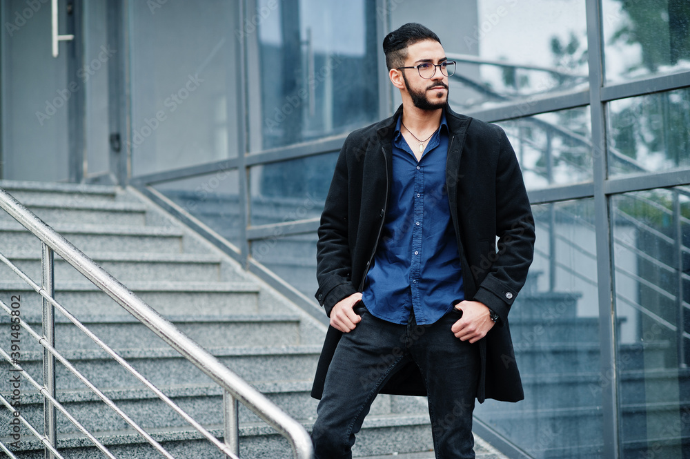 Middle eastern entrepreneur wear black coat and blue shirt, eyeglasses against office building, stand on stairs. Middle eastern entrepreneur wear black coat and blue shirt, eyeglasses against office building, stand on stairs.