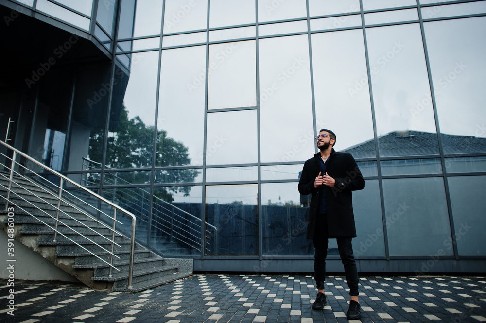 Middle eastern entrepreneur wear black coat and blue shirt, eyeglasses against office building. Middle eastern entrepreneur wear black coat and blue shirt, eyeglasses against office building.
