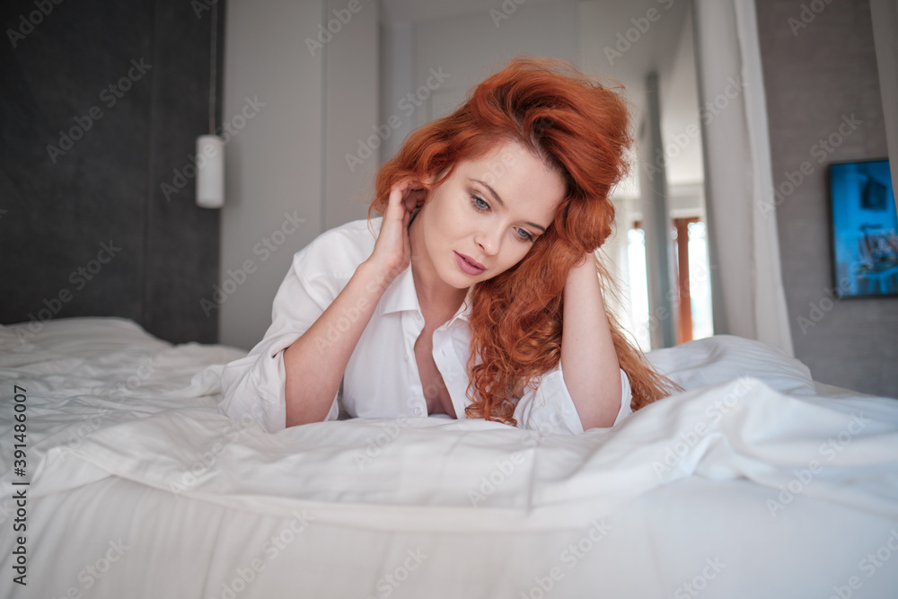 cute red hair woman in white shirt relax on the bed in her white room