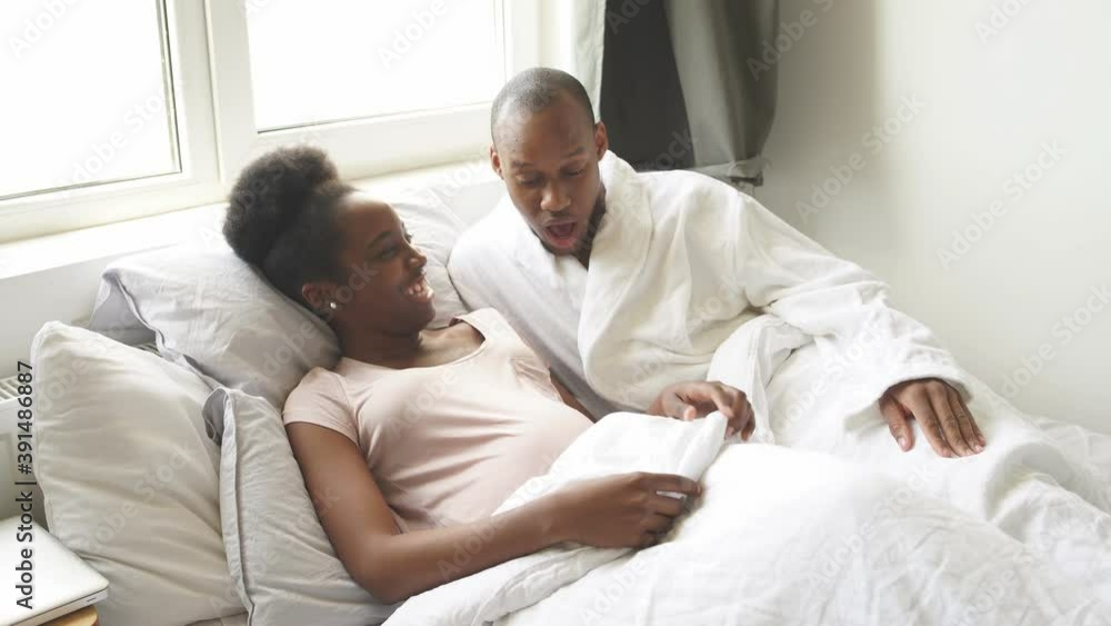 Happy black man surprisingly looks at pregnant wife's belly, man is in shock, every day baby in stomach becomes bigger and bigger, they lie on bed together. Happy black man surprisingly looks at pregnant wife's belly, man is in shock, every day baby in stomach becomes bigger and bigger, they lie on bed together.