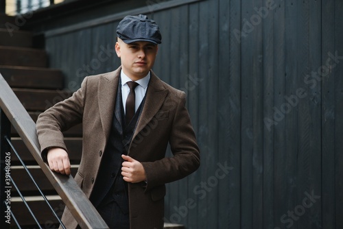 Canvas Print A man posing in the image of an English retro gangster of the 1920s dressed in a coat, suit and flat cap in Peaky blinders style