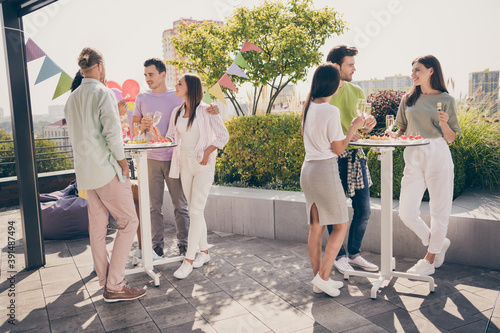Canvas Print Full body portrait of beautiful fellows stand around table hands hold champagne