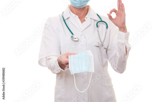 Young doctor in white uniform and stethoscope wearing mask and showing ok sign on isolated background
