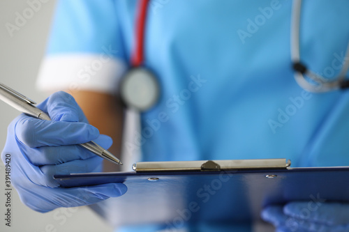 Photos Doctor's hand in gloves holds pen and fills out documents on clipboard