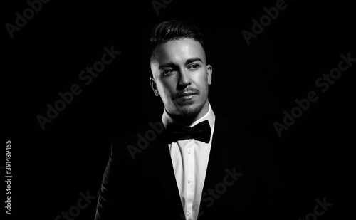 Handsome young man in suit and bow tie posing on black background in black and white