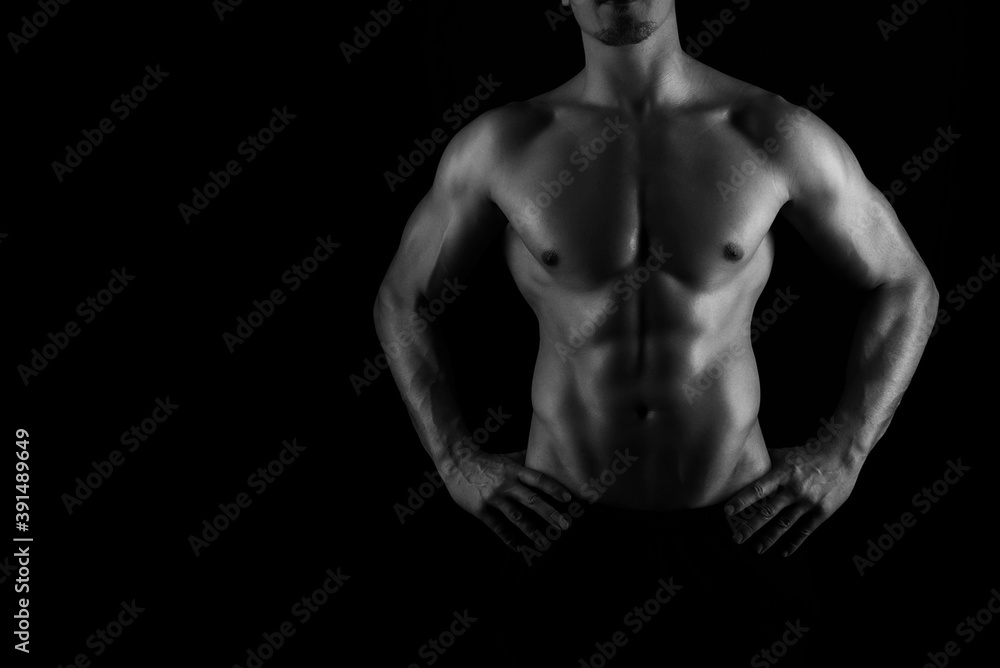 Muscular male torso of fit bodybuilder on black background in black and white Muscular male torso of fit bodybuilder on black background in black and white