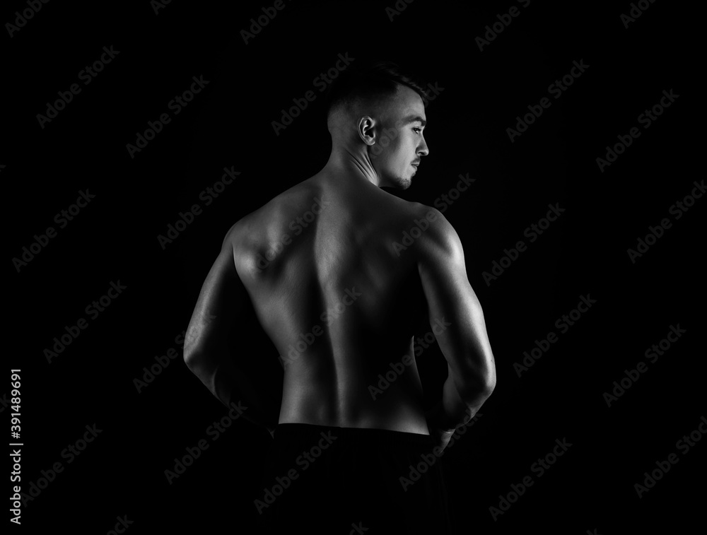 Fototapeta premium Muscular male torso of fit bodybuilder on black background in black and white