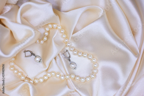 Pearl necklace and pearl earrings on beige silk, top view. Jewelry for the bride