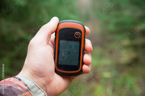 Man's hand holds tourist GPS navigator. Green trees in the background.