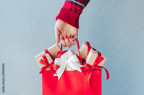 Cropped image of female hand with red polished nails holding shopping bag full of christmas gift boxes