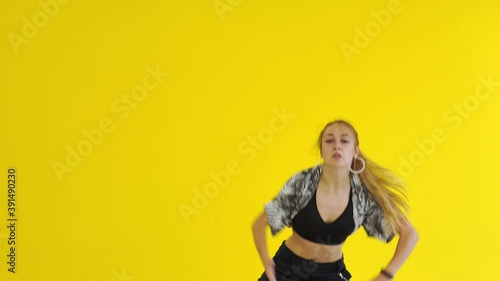 Young energetic woman dancing modern youth dance free style in the studio against the background of a yellow wall. Isolated. Medium long shot