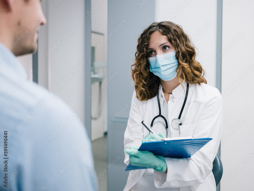 Junge Ärztin geht den Anamnesebogen mit einem neuen Patienten durch Junge Ärztin geht den Anamnesebogen mit einem neuen Patienten durch