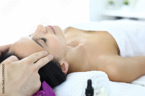 Woman lies on massage table with her eyes closed masseur does an acupressure face massage. Rejuvenation services in beauty salons concept