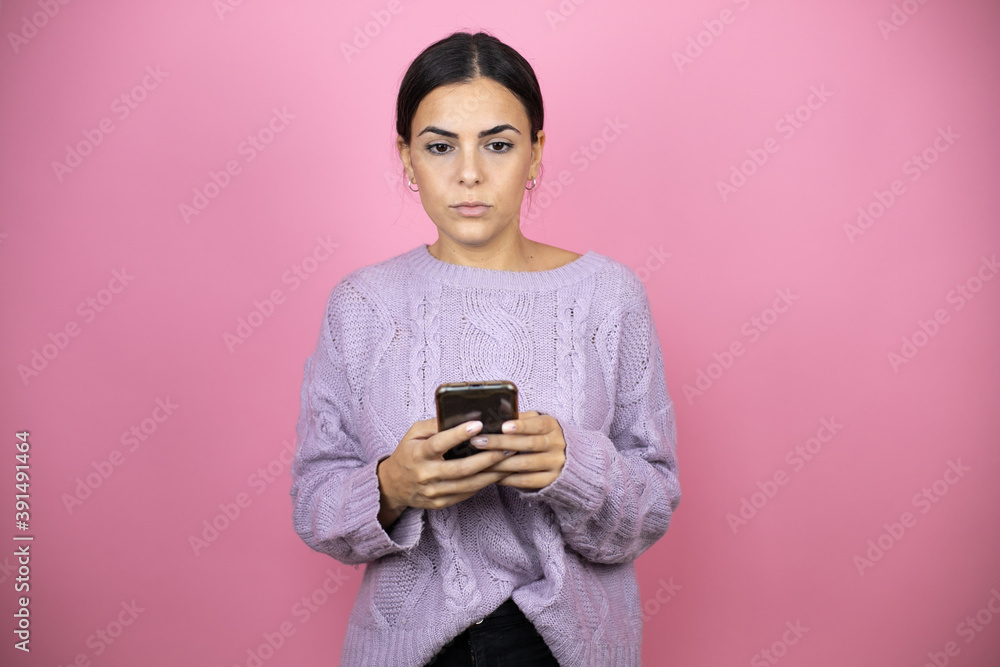 Beautiful woman wearing a casual violet sweater over pink background texting with her phone Beautiful woman wearing a casual violet sweater over pink background texting with her phone