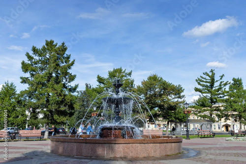 Kostroma. Fountain in the square on Sovetskaya square. Water splashes against the background of larch trees and blue sky.
