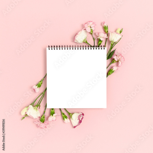 Blank notepad mockup with frame made of flowers. Greeting card concept on a pink pastel background. © rorygezfresh