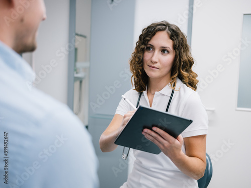 Принти на полотні Junge Ärztin geht den Anamnesebogen mit einem neuen Patienten durch