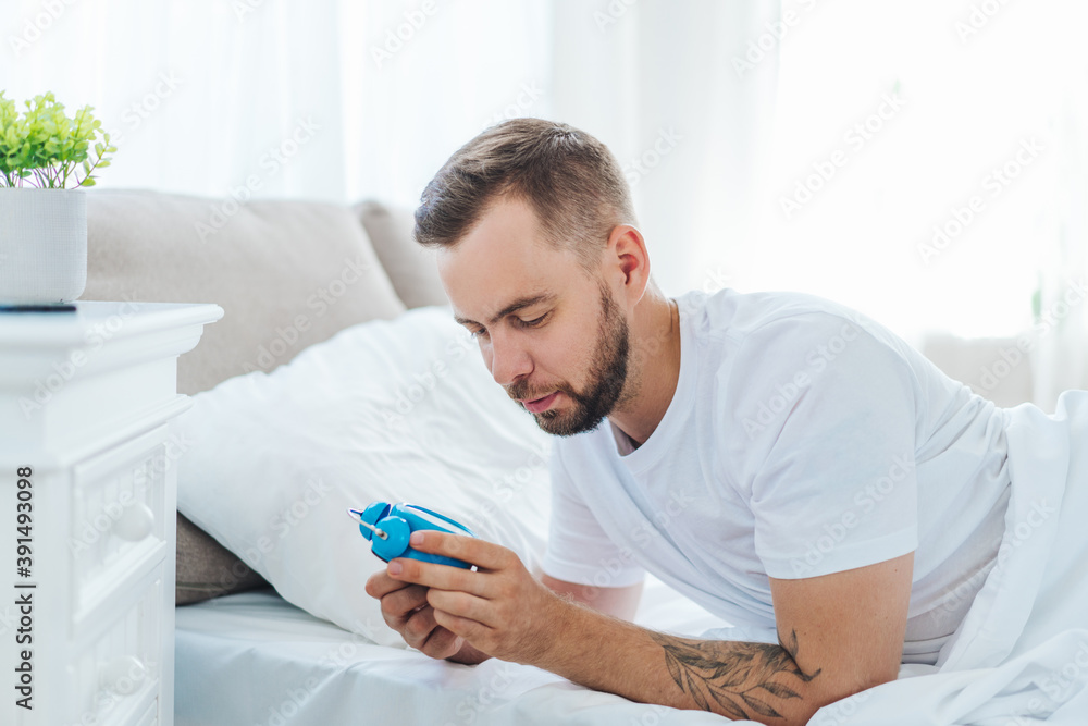 Portrait of young bearded man turning off the alarm clock while lying in the bed at home Portrait of young bearded man turning off the alarm clock while lying in the bed at home