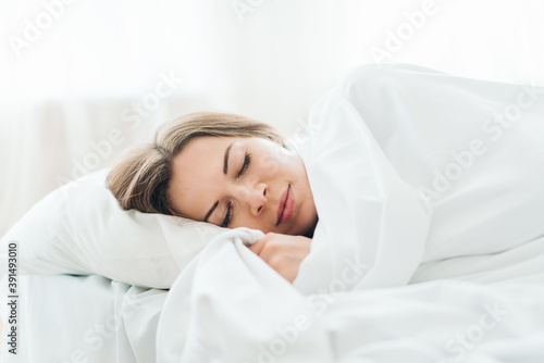 Portrait of a young woman sleeping in cozy light colored bedroom lying in the bed with eyes closed