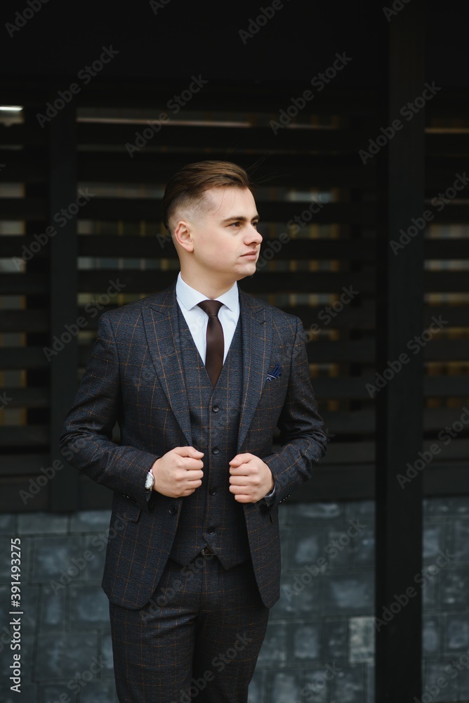 Fototapeta premium Portrait of handsome fashion businessman model dressed in elegant suit. Man posing on street background. Metrosexual