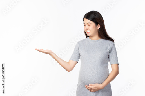 Young beautiful pregnant woman stand and touching belly showing empty copy space on the open hand palm for text on white background. Pregnancy, motherhood, people and expectation concept.