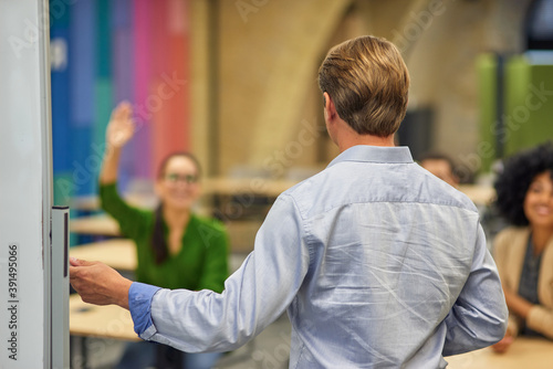 Rear view of a male coach or speaker pointing at giving a presentation to audience during corporate seminar or training, selective focus