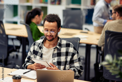 Young happy mixed race man reading notes while working in the modern office, selective focus