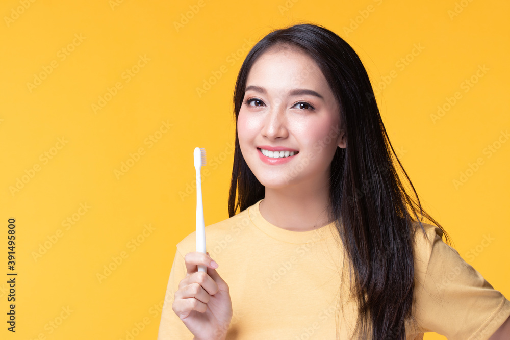 Beauty portrait young asian woman holding toothbrush and smiling on yellow background. Concept good oral and dental health.