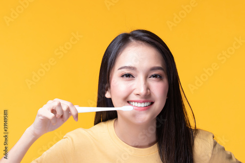 Beauty portrait young asian woman holding toothbrush and smiling on yellow background. Concept good oral and dental health.