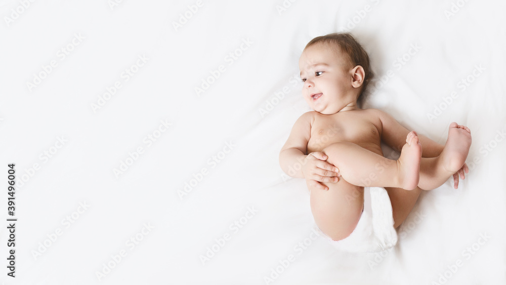 Funny little kid wearing in diaper. Portrait of a cute baby 6 months old lying on a white blanket. Beautiful toddler. Child after bath or shower on a fresh towel.Cute kid playing with his feet. Funny little kid wearing in diaper. Portrait of a cute baby 6 months old lying on a white blanket. Beautiful toddler. Child after bath or shower on a fresh towel.Cute kid playing with his feet.