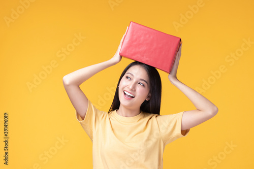 Portrait of happy smiling girl in casual holding gift box and expression face isolated over yellow background