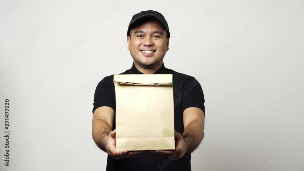 Asian delivery man in black uniform holding the paper bag giving to customer on isolated white background. 4k Resolution. Asian delivery man in black uniform holding the paper bag giving to customer on isolated white background. 4k Resolution.