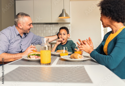 Smiling mixed race family sitting at the kitchen table having breakfast at home. 