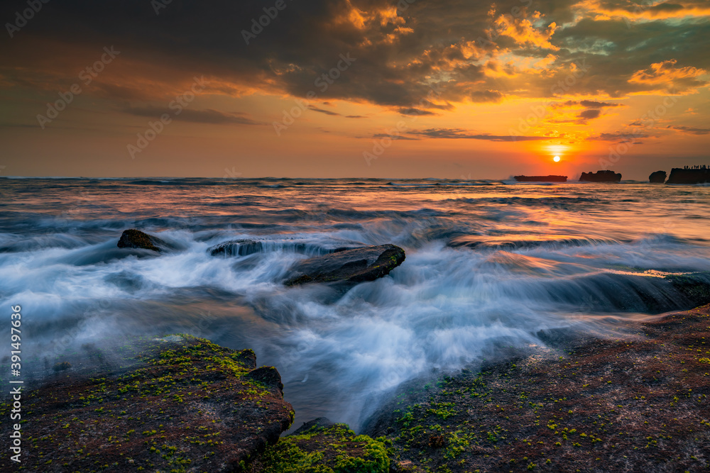 Beautiful seascape. Sunset scenery background. Moving waves. Low tide at the beach. Composition of nature. Cloudy sky with sunlight. Slow shutter speed. Mengening beach, Bali, Indonesia