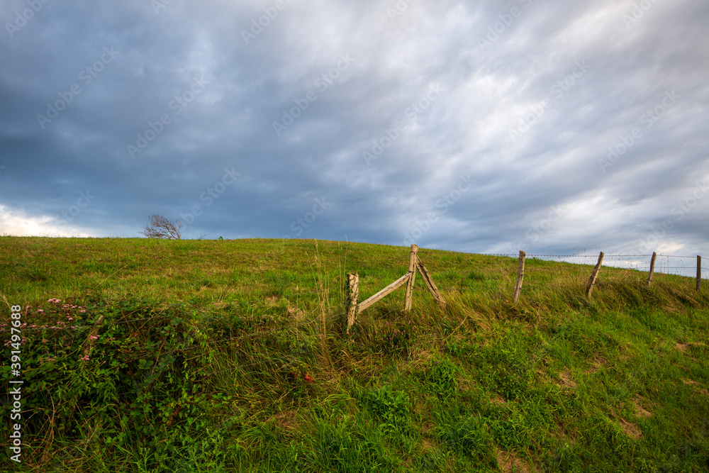 Angular view of blue sky with white clouds, hawthorn fence and green meadows in a town in Cantabria, Spain, horizontal